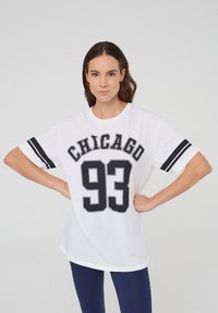 T-shirt bianco con la scritta "CHICAGO" e il numero "93" in nero, con strisce nere sulle maniche e una vestibilità rilassata. Tessuto di cotone liscio.