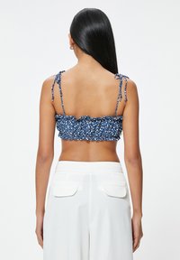 Top corto de estampado azul con un borde con volantes, tirantes finos atados y un diseño de espalda fruncida, combinado con pantalones blancos de cintura alta.