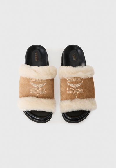 Hellbraune Wildleder-Slides mit cremefarbenem Kunstfellbesatz. Verfügen über dekorative Nähte am Riemen und schwarze Gummisohlen. Glatte Textur.