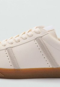 Sneaker in pelle beige con dettagli in suede grigio chiaro, punta rotonda, occhielli bianchi e suola in gomma con una leggera texture.