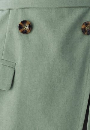 Light green fabric with a textured finish, featuring two round, patterned brown buttons and a side pocket detail.