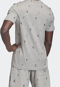 Szara bawełniana koszulka z krótkim rękawem, z powtarzającym się wzorem logo w czerni i bieli. Lekko luźny krój, gładki tył.