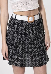 Falda negra con bordados florales blancos, con un dobladillo con volantes. Combinada con un cinturón blanco en contraste y una hebilla rectangular.