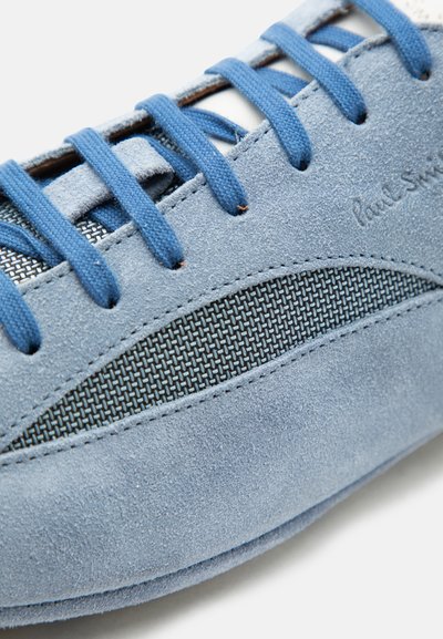 Gros plan d'une basket en daim bleu avec des lacets bleus et un panneau en tissu texturé sur le côté.