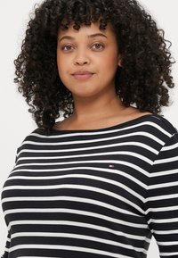 Czarna i biała, paskowana koszula z miękkiego materiału, z łódkowym dekoltem i małym logo po lewej stronie. Krótkie rękawy.