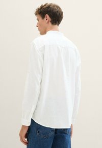 Weißes Langarmhemd aus leichtem Leinen, mit Button-Down-Kragen, geknöpften Ärmeln und entspannter Passform. Subtile Textur sichtbar.