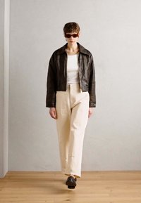 Black leather cropped jacket over a white sleeveless top, paired with cream wide-leg pants and dark shoes, showcased against a neutral backdrop.