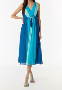 Femme portant une robe midi sans manches à col en V, colorée en bloc bleu avec une ceinture à la taille, assortie à des talons à brides bleu clair.