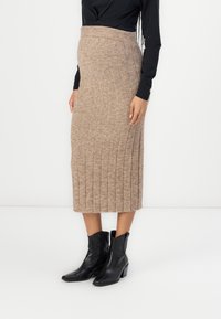 Gonna midi in maglia beige con texture a coste e vita aderente. Abbinata a stivaletti neri alla caviglia, che evidenziano la lunghezza e il design della gonna.