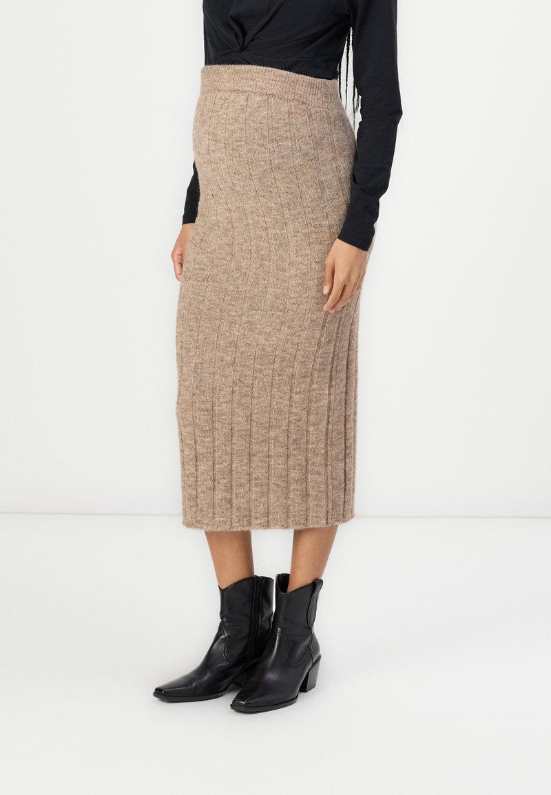 Gonna midi in maglia beige con texture a coste e vita aderente. Abbinata a stivaletti neri alla caviglia, che evidenziano la lunghezza e il design della gonna.