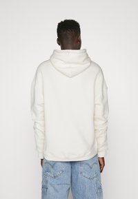 Sudadera blanca con bolsillo tipo canguro, corte holgado, puños y dobladillo acanalados. Combinada con jeans cargo azul claro que presentan grandes bolsillos.