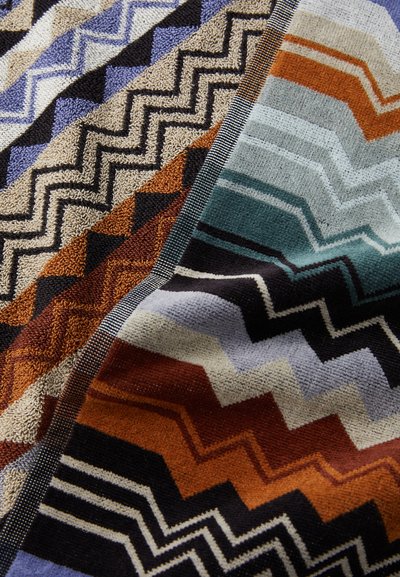 Vezenina z multicolornimi geometrijskimi vzorci z zigzag oblikami v zemeljskih tonih, modrih barvah in strukturirano površino. Mehka, puhaste material.
