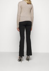 Beige gestrickter Pullover mit gerippten Bündchen, kombiniert mit schwarzen ausgestellten Hosen und schwarz-weiß gemusterten High Heels.