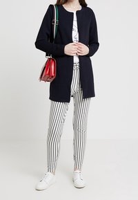 Marinblå ribbad kofta med rund krage, kombinerad med svart- och vitrandiga tajta byxor och vita sneakers. Röd handväska som accent.