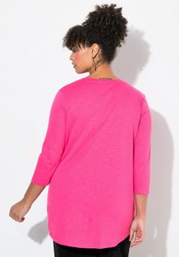 Langarmshirt mit Rundhalsausschnitt aus leuchtend rosa Stoff, mit einem lockeren Schnitt und einem abgerundeten Saum hinten. Geschmeidige Textur.