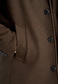 Cappotto di lana marrone con un design elegante, bottoni neri e una tasca laterale con una texture morbida.