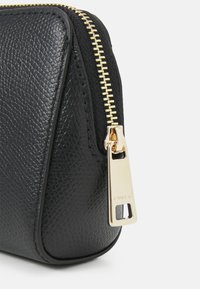 Black textured leather pouch with a gold zipper. Features a metal pull tab embossed with "FURLA" and a rounded base design.