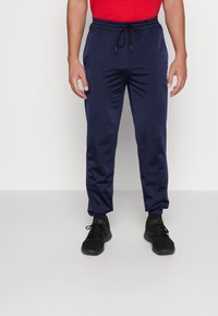 Marineblå træningsbukser lavet af skinnende materiale, med elastisk talje, justerbar snøre og tapered manchetter.