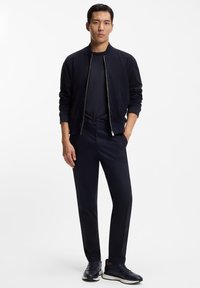 Marineblaue Bomberjacke aus Wildleder über einem marineblauen T-Shirt, kombiniert mit maßgeschneiderten marineblauen Hosen und dunklen Sneakers. Einfaches, elegantes Design ohne Muster.