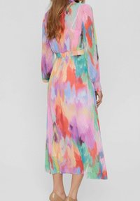Robe longue et colorée mêlant des nuances de rose, orange, vert et bleu. Tissu transparent à pois, taille smockée et manches longues.