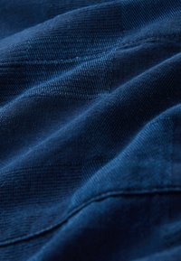 Tissu texturé bleu foncé avec un motif à carreaux, présentant des fibres tissées douces et des coutures visibles le long des bords.