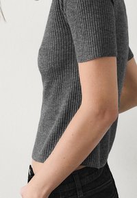 Szary prążkowany krótki top z krótkimi rękawami, o dopasowanym kroju i gładkiej fakturze, zestawiony z ciemnymi spodniami denimowymi.