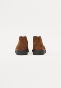 Bruine suede enkelboots met een gladde oppervlakte, ronde neus en een zwarte rubberen zool. Bevat zichtbare stiksels langs de basis.