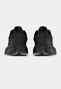 Μαύρα αθλητικά παπούτσια με υφασμάτινο συνθετικό επάνω μέρος με υφή, στρογγυλές λαστιχένιες σόλες και θηλιές στο πίσω μέρος, με λείο φινίρισμα και ελάχιστες λεπτομέρειες.