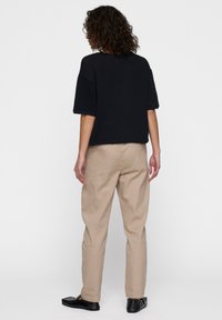 Zwarte top met korte mouwen en een losse pasvorm, gecombineerd met beige broek. De broek heeft een ontspannen silhouet en een lichte tapering bij de enkels.