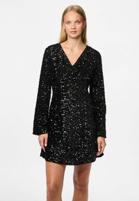 Vestido negro de manga larga cubierto de lentejuelas, con escote en V profundo, cintura ajustada y dobladillo acampanado, que muestra una superficie brillante y texturada.