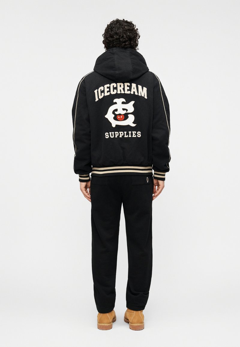 Μαύρο φούτερ με κουκούλα με το κείμενο "ICECREAM SUPPLIES" και γραφικό στην πλάτη, συνδυασμένο με μαύρο παντελόνι και ταμπά μποτάκια. Ριμπ μανσέτες και τελείωμα.