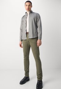 Camisa de botones gris con estampado, jersey de cuello alto color crema, pantalones verde oliva y mocasines negros. Las características incluyen botones, corte ajustado y texturas suaves.