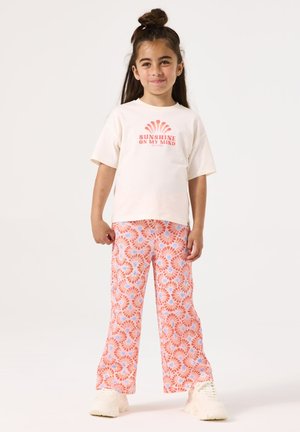 Crème t-shirt met de opdruk "SUNSHINE ON MY MIND", gecombineerd met roze gestreepte broek met blauwe en rode bloemmotieven. Witte sneakers.
