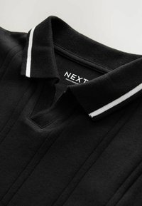 Polo nera con scollo a V, caratterizzata da un tessuto texturizzato e un colletto a coste decorato con righe bianche. Etichetta "NEXT" visibile all'interno.