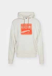 Sudadera de color crema con un bolsillo frontal, que presenta un gráfico cuadrado naranja con montañas y texto. Incluye capucha con cordón.