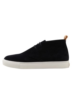 Sort ruskind high-top sneaker med hvid gummisål og brun trække-flap bagpå, vist fra siden på hvid baggrund.
