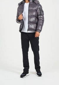 Grå puffjacka med glänsande yta, dragkedjestängning och avtagbar huva. I kombination med svarta byxor och svarta sneakers.