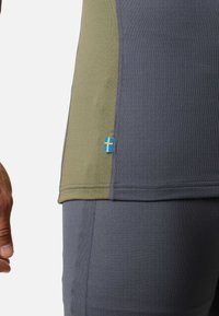 Fitted athletic top with gray and olive green panels. Features a small blue and yellow flag detail. Textured fabric, smooth stitching.