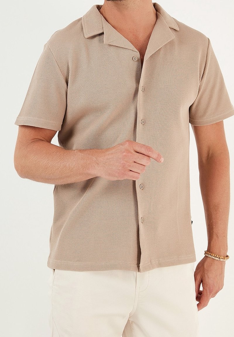 Kortärmad, knäppskjorta i ljusbeige med en ribbad textur och klassisk krage. Tyget är mjukt och lätt.
