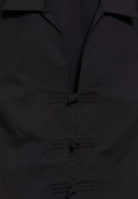 Manteau noir de face présentant trois fermetures à boutons traditionnels chinois en forme de grenouille et un large col.