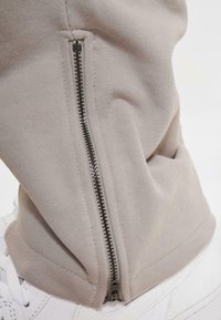 Beige joggebukser med en sort lynlås langs sidesømmen, ribbede manchetter og en blød, glat tekstur. Stylet med hvide sneakers.