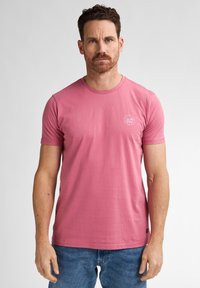 T-shirt rosa a maniche corte in cotone, con scollo rotondo e una piccola grafica stampata sul petto. Vestibilità casual e texture liscia.