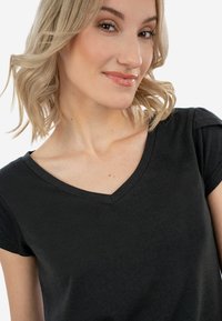 Černé tričko s V-výstřihem vyrobené z měkké bavlny, s krátkými rukávy, jemným detailem na ramenech a přiléhavým střihem pro elegantní vzhled.