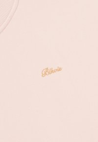 Débardeur rose pâle en tissu doux, avec un col côtelé et un petit logo textuel brodé en or à l'avant.