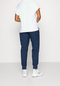 Mörkblå joggers med avsmalnande ben, elastiska muddar och sidofickor, tillsammans med en vit kortärmad skjorta och vita sneakers.