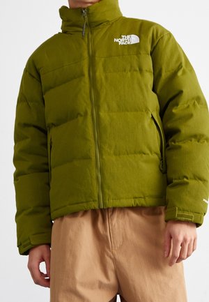 Groene gewatteerde North Face-jas met ritssluiting aan de voorkant, ritssluitingen aan de zijkanten en verstelbare polsbanden, gedragen met beige broek.