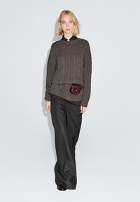 Brun, ribbet sweater over en bordeaux skjorte, parret med mørkt stribede brede bukser. En lille brun pung er fastgjort ved taljen.
