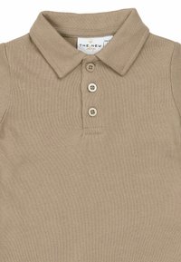 Bordinis polo marškinėlis smėlio spalvos, su apykakle, trimis rudos spalvos mygtukais ir faktūriniu audiniu. Prekės ženklo etiketė matoma po apykakle.