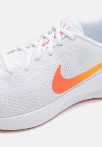 White athletic shoe with textured mesh upper. Features a bright orange Nike swoosh and contrasting orange accent on the sole.