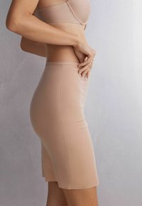Nude bezszwowy kombinezon o dopasowanym kroju, miękkiej teksturze i długości do połowy uda. Posiada gładki pas w talii oraz sylwetkę podkreślającą kształty.